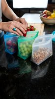 Woman organizing fresh produce and nuts into reusable storage containers on kitchen counter for meal prep and pantry organization.