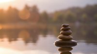 Zen stone stack balanced on water surface at sunset with warm golden light and peaceful lake reflection creating meditation and mindfulness atmosphere.