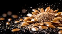 Golden sunflower seeds scattered on black background with water drops and dramatic lighting creating artistic food composition with bokeh effect.