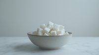 White sugar cubes stacked in ceramic bowl on marble surface against neutral background, minimalist food composition for healthy lifestyle and dietary concepts.