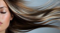 Young woman with flowing highlighted brown hair against dark background, eyes closed in serene expression, showing natural hair movement and professional salon styling.