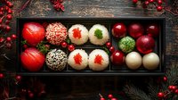 Festive assortment of colorful cake pops and dessert balls decorated with sprinkles, caviar and herbs in wooden box on dark rustic background with red berries.