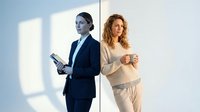 Two professional businesswomen in modern office setting with natural lighting. One in dark suit holding tablet, another in casual beige outfit with coffee cup.
