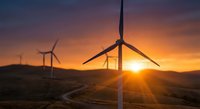 Wind turbines generating clean renewable energy at sunset with dramatic orange sky and mountain landscape for sustainable power concepts.