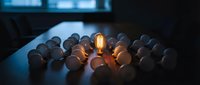 Glowing vintage Edison bulb surrounded by unlit bulbs on dark surface symbolizing innovation, creativity, leadership and unique ideas standing out from crowd.