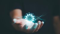 Person holding glowing gear icon with digital particles, representing technology, innovation, and engineering solutions for business and industrial applications.