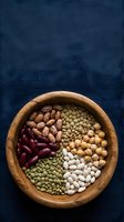 Assorted legumes and beans in wooden bowl on dark blue textile background for healthy cooking and nutrition concepts.