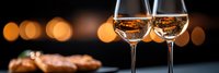 Two elegant wine glasses filled with white wine against warm bokeh lights creating romantic dining atmosphere for celebration or date night.