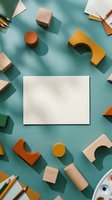 Blank white card mockup surrounded by colorful wooden toy blocks and pencils on teal background, flat lay with copy space for text.