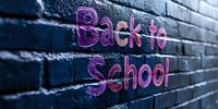 Pink neon glowing back to school text written on dark brick wall background creates modern urban street art atmosphere for education concept.