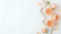Elegant peach roses with silk ribbon and scattered petals on white background for wedding invitations and romantic design projects.