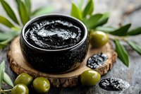 Black caviar served in ceramic bowl on wooden slice with fresh green olives and leaves, luxury gourmet appetizer on dark stone background.