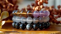 Healing crystal bracelets with amethyst, clear quartz and black obsidian beads stacked on wooden surface with soft bokeh background and autumn leaves.