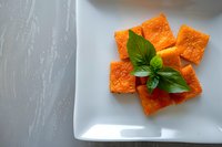 Fresh salmon cubes garnished with basil leaves on white plate. Raw fish portions prepared for cooking or sashimi serving in modern kitchen setting.