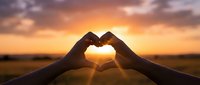 Hands forming heart shape silhouette against golden sunset sky with warm sunlight streaming through fingers creating romantic love symbol during magic hour.