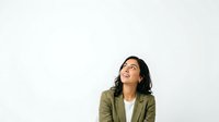 Young woman with dark hair and South Asian ethnicity wearing olive green blazer over white top, looking upward with thoughtful expression against white background, isolated for design use.