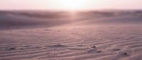 Serene desert landscape at sunset with soft pink and purple tones, gentle sand dunes, and warm golden light breaking through clouds for travel and nature backgrounds.