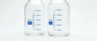 Two clear glass laboratory beakers with measurement markings and blue liquid samples isolated on white background for scientific research and education.