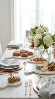 Elegant brunch table setting with white hydrangeas, pastries, cheese board and crystal glasses in bright dining room for entertaining guests.