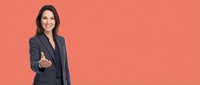 Professional businesswoman in dark suit giving thumbs up gesture against coral background, confident corporate executive showing positive attitude.