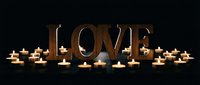 Wooden LOVE letters surrounded by glowing tea light candles on dark background, creating warm romantic atmosphere for Valentine's Day or wedding decor.