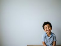 Young boy with dark hair and olive complexion, wearing light blue polo shirt, smiling at camera against neutral white background. Suitable for educational materials, child development content, and family-oriented designs.