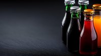 Colorful glass bottles with condensation on dark slate background, selective focus with copy space for beverage marketing and product photography.