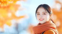 Young Asian woman wearing orange knitted scarf smiling outdoors during autumn season with golden foliage bokeh background creating warm seasonal mood.
