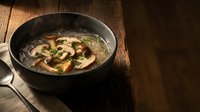 Hot mushroom soup with fresh herbs in black pan on rustic wooden table, comfort food for cold weather dining and restaurant menu photography.