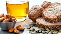Fresh sliced whole grain bread with almonds, walnuts, pumpkin seeds and honey in glass on rustic wooden table. Healthy breakfast concept.
