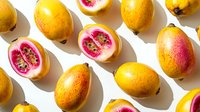 Fresh ripe guava fruits whole and cut in half showing pink flesh and seeds arranged on white background with natural shadows.