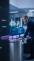 Middle-aged Caucasian businessman analyzing cloud computing data on monitors in modern office with holographic interface elements and digital analytics dashboard.