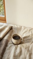 Cozy morning coffee cup on rumpled bed linens with warm sunlight streaming through window creating peaceful bedroom atmosphere for relaxation and comfort.