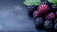Fresh ripe blackberries with green leaves on dark textured background, selective focus with copy space for food photography and menu design.