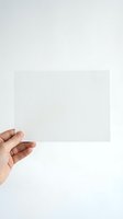 Hand holding blank white paper sheet against neutral background for mockup design and presentation purposes.