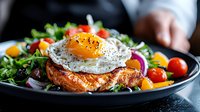 Grilled salmon fillet topped with sunny side up egg, served with fresh mixed greens, cherry tomatoes, and colorful bell peppers on dark plate.