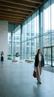 Professional businesswoman walking through modern corporate office lobby with floor-to-ceiling windows and contemporary architecture for business concepts.