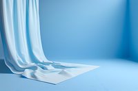 Elegant white fabric draping over surface against light blue background creates soft flowing curves and gentle shadows for minimalist composition.