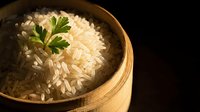 Steamed white rice with fresh parsley garnish served in traditional bamboo steamer basket on dark background for Asian cuisine and healthy cooking concepts.