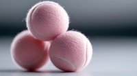 Pink tennis balls stacked in pyramid formation on white surface with soft lighting for sports and recreation themes.