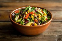 Fresh mixed vegetable salad with chickpeas and colorful ingredients in terracotta bowl on rustic wooden table, healthy Mediterranean cuisine served.
