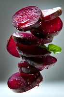Fresh sliced beetroot stacked in creative composition with water drops and green leaf on gray background, macro food photography for healthy eating.