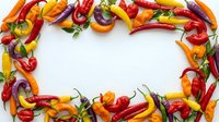 Colorful hot chili peppers frame border on white background with copy space for text. Fresh spicy vegetables arrangement for cooking and food design.