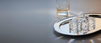 Glasses of water and whiskey on white plate with dark surface, suitable for beverage, hospitality, and restaurant design projects.