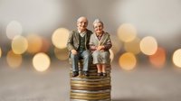 Senior couple figurines sitting on stack of coins with bokeh lights background representing retirement planning and financial security.