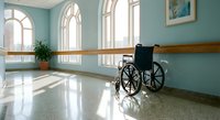 Empty wheelchair in bright hospital corridor with arched windows and natural light streaming across polished floors in healthcare facility.