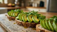 Sliced avocado on whole grain toast with fresh herbs, arranged on wooden cutting board in bright kitchen setting for food photography and healthy eating content.