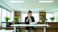 Professional businesswoman reviewing documents at modern office desk with plants and natural lighting for corporate presentations.