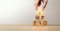 Hand placing wooden cube with lightbulb icon on stack of blocks featuring AI, gear, question mark, magnifying glass and target symbols on desk.
