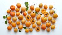 Apricots arranged flat lay on white background, whole and halved fruits with pits visible and green leaves, overhead view for food styling and culinary content.